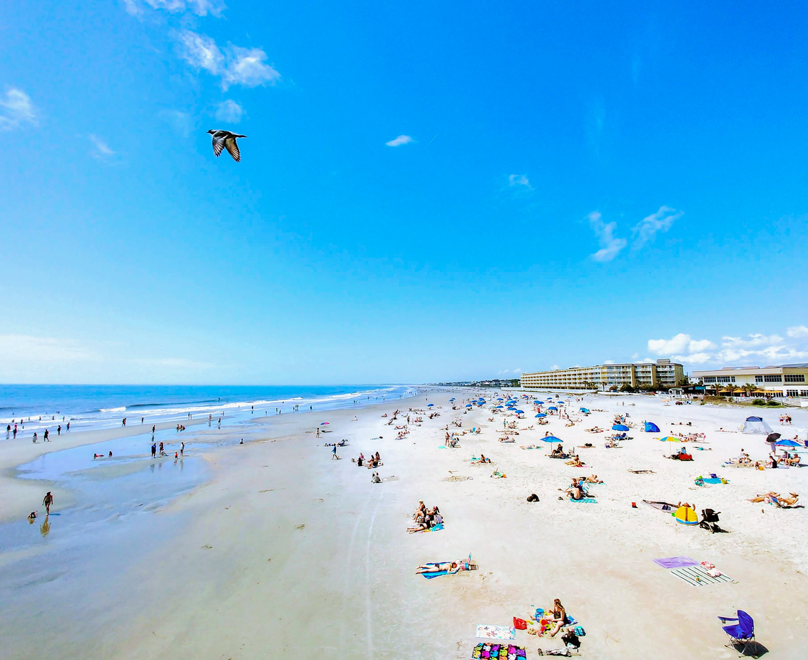 View of Folly Beach along the Charleston Coast full of beach vacationers and a kite flying in the sky.